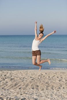 Girl young cheerful woman jumping in the air on the beach in the sand in the morning on the sea in summer vacation