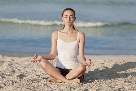 Young sporty woman doing sport yoga on the beach in the sand on the beach in the sun