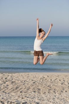 Girl young cheerful woman jumping in the air on the beach in the sand in the morning on the sea in summer vacation