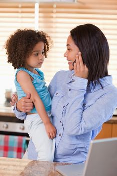 Young mother and daughter using cellphone in the kitchen