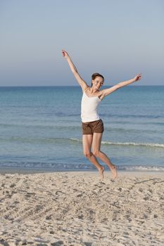 Girl young cheerful woman jumping in the air on the beach in the sand in the morning on the sea in summer vacation