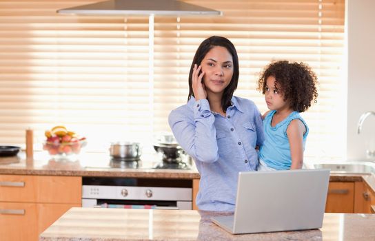 Young mother and daughter with cellphone and laptop in the kitchen together