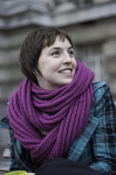 Pretty woman with a lovely smile sitting outdoors in grey wintery weather dressed against winter cold in a thick coat and scarf