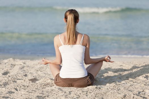 Young sporty woman doing sport yoga on the beach in the sand on the beach in the sun