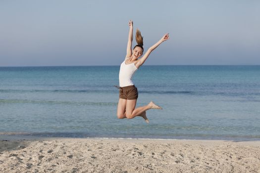 Girl young cheerful woman jumping in the air on the beach in the sand in the morning on the sea in summer vacation