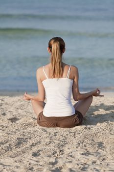 Young sporty woman doing sport yoga on the beach in the sand on the beach in the sun