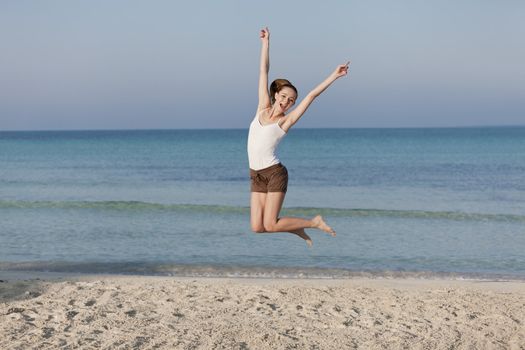 Girl young cheerful woman jumping in the air on the beach in the sand in the morning on the sea in summer vacation