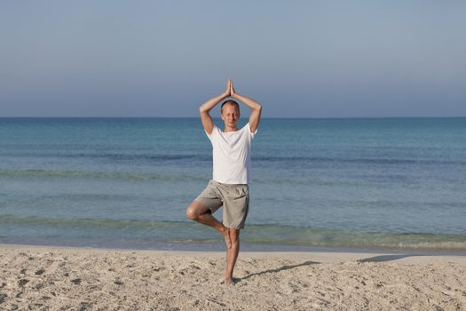 Young athletic man doing sport yoga on the beach in the sand on the beach in the sun