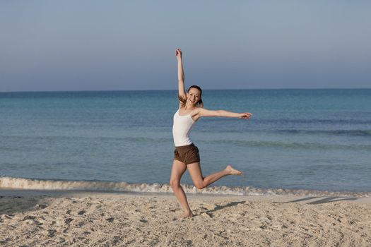 Girl young cheerful woman jumping in the air on the beach in the sand in the morning on the sea in summer vacation