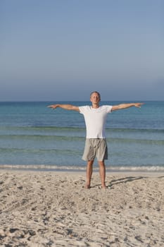 Young athletic man doing sport yoga on the beach in the sand on the beach in the sun
