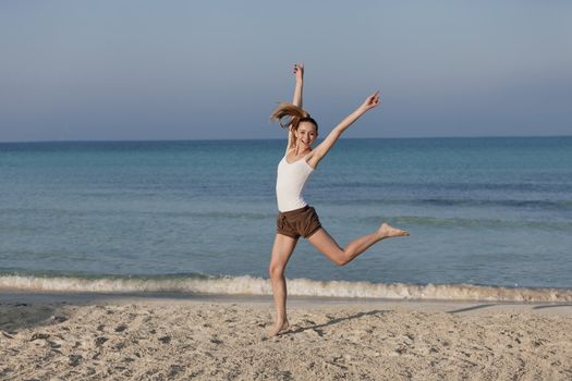 Girl young cheerful woman jumping in the air on the beach in the sand in the morning on the sea in summer vacation