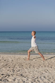 Young athletic man doing sport yoga on the beach in the sand on the beach in the sun