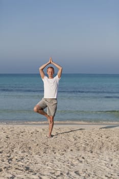 Young athletic man doing sport yoga on the beach in the sand on the beach in the sun