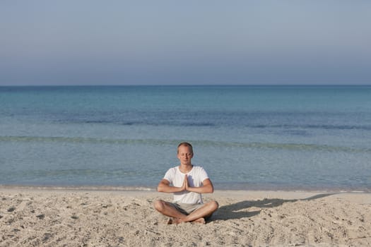 Young athletic man doing sport yoga on the beach in the sand on the beach in the sun