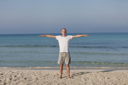 Young athletic man doing sport yoga on the beach in the sand on the beach in the sun