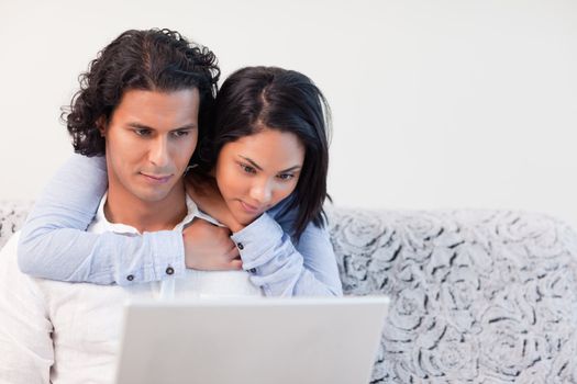 Young woman hugging her boyfriend that is working on his notebook