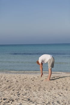 Young athletic man doing sport yoga on the beach in the sand on the beach in the sun