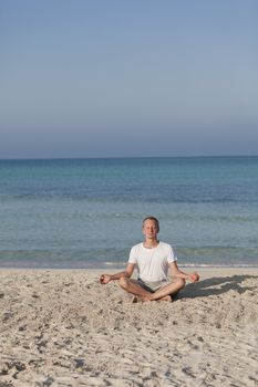 Young athletic man doing sport yoga on the beach in the sand on the beach in the sun