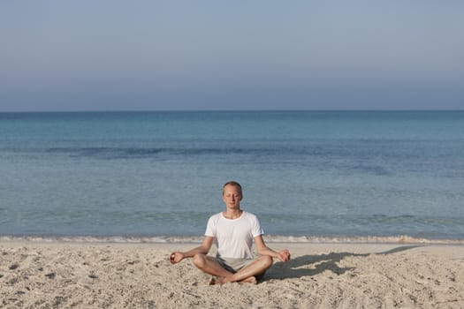 Young athletic man doing sport yoga on the beach in the sand on the beach in the sun