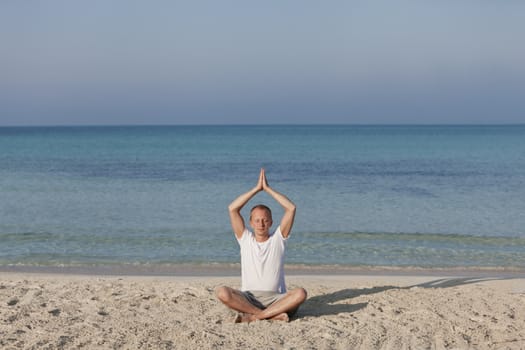 Young athletic man doing sport yoga on the beach in the sand on the beach in the sun