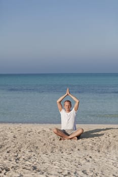 Young athletic man doing sport yoga on the beach in the sand on the beach in the sun