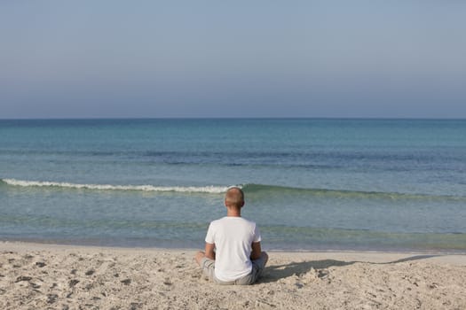 Young athletic man doing sport yoga on the beach in the sand on the beach in the sun