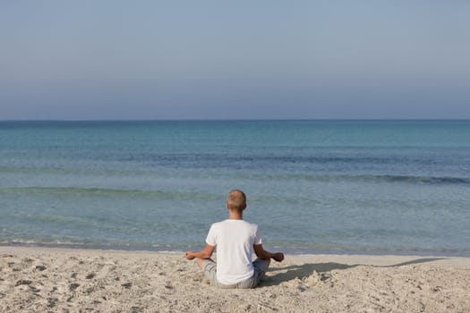 Young athletic man doing sport yoga on the beach in the sand on the beach in the sun