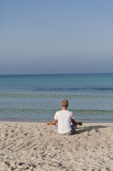 Young athletic man doing sport yoga on the beach in the sand on the beach in the sun