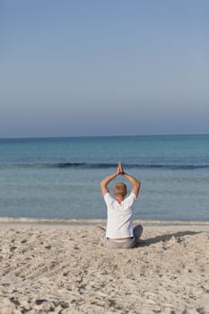 Young athletic man doing sport yoga on the beach in the sand on the beach in the sun
