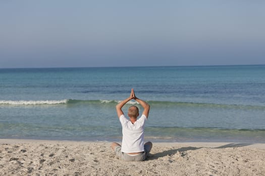 Young athletic man doing sport yoga on the beach in the sand on the beach in the sun