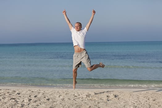 Young happy young man jumping in the air on the beach in the sand in the morning on the sea in summer vacation