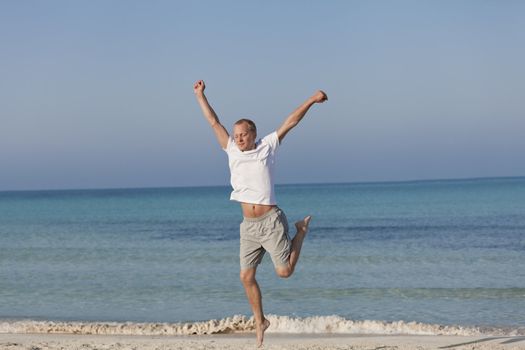 Young happy young man jumping in the air on the beach in the sand in the morning on the sea in summer vacation
