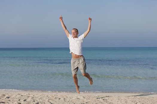 Young happy young man jumping in the air on the beach in the sand in the morning on the sea in summer vacation