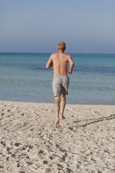 Young man running on the beach young running in water with splashes and fun in the summer holidays
