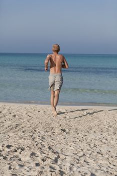 Young man running on the beach young running in water with splashes and fun in the summer holidays