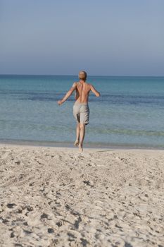 Young man running on the beach young running in water with splashes and fun in the summer holidays