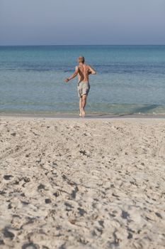 Young man running on the beach young running in water with splashes and fun in the summer holidays