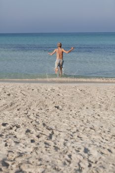 Young man running on the beach young running in water with splashes and fun in the summer holidays