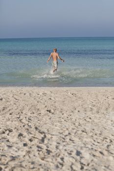 Young man running on the beach young running in water with splashes and fun in the summer holidays