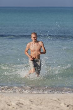 Young man running on the beach young running in water with splashes and fun in the summer holidays