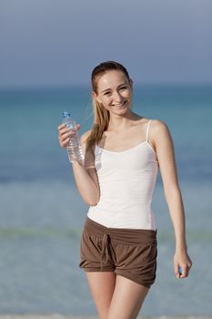 Girl young woman refreshing drinks water from a bottle on the beach by the sea in summer vacation