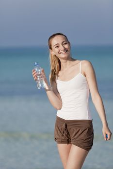 Girl young woman refreshing drinks water from a bottle on the beach by the sea in summer vacation