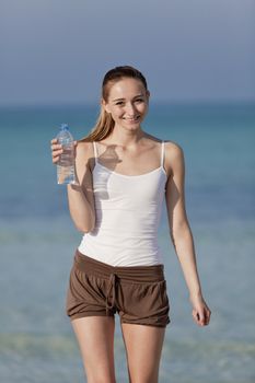 Girl young woman refreshing drinks water from a bottle on the beach by the sea in summer vacation