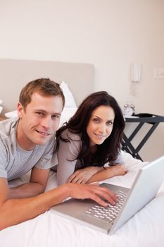 Smiling young couple using laptop in the bedroom together