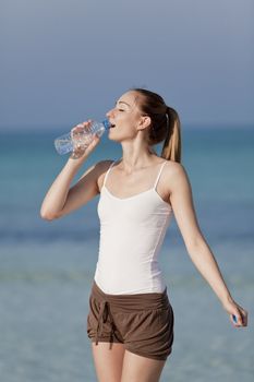 Girl young woman refreshing drinks water from a bottle on the beach by the sea in summer vacation