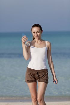 Girl young woman refreshing drinks water from a bottle on the beach by the sea in summer vacation