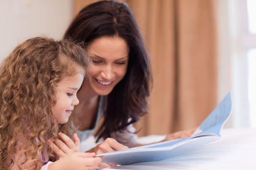 Side view of young mother and daughter reading a book together