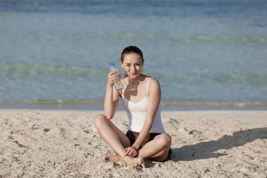 Girl young woman refreshing drinks water from a bottle on the beach by the sea in summer vacation