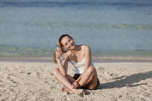 Girl young woman refreshing drinks water from a bottle on the beach by the sea in summer vacation