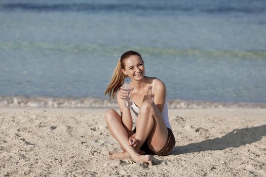 Girl young woman refreshing drinks water from a bottle on the beach by the sea in summer vacation